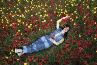 Young happy girl resting in the field of red poppy flowers. Drone aerial of woman in spring