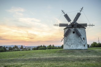 Windmill with wooden sails in a landscape with fields. Meadows and flowers appear in the sunset.