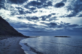 Sunset on the Danish coast. Beach, waves. Hill with trees in background. Landscape photo from sea