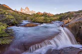 A waterfall with the Fitz Roy mountain illuminated by the morning sun in the Los Glaciares National