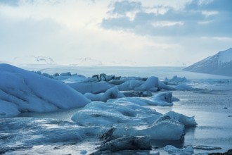 Expansive view of ice floes with mountains and ocean under a clearing sky, iceberg Iceland,