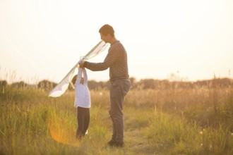 Dad helps his daughter to fly a kite in a field in the summer at sunset. Family entertainment