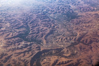Aerial view of a vast, reddish desert landscape with river valleys and hilly areas, The dunes of