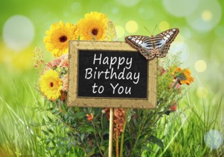 An image of a little chalkboard in the garden with the text happy birthday to you
