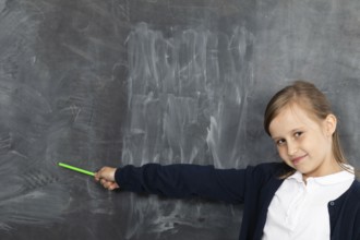 Schoolgirl shows on an empty school board. He is standing in the classroom at the chalkboard.