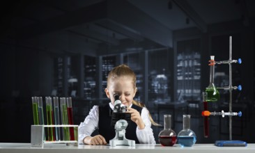 Little girl scientist looking through microscope in classroom at chemistry lesson. School chemical