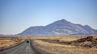 A car drives on a dusty road towards a towering mountain in the background, By car through the