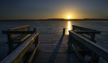 Wooden jetty with benches on a frozen lake in the light of the golden rising sun, beautiful