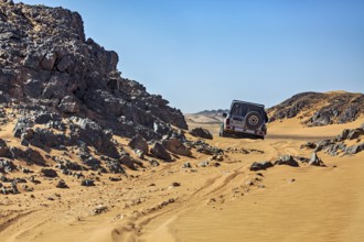 An off-road vehicle drives through a rocky desert landscape under a bright blue sky, off-road by