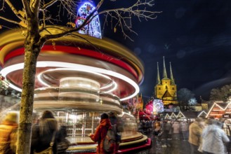 Lebhafte Szene eines Weihnachtsmarktes bei Nacht mit einem Karussell in Bewegung und Kirchtürmen im