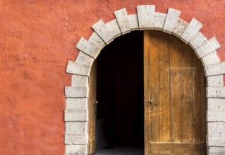 Antique arched entrance with double wooden doors, left side opened, and the orange-pink wall