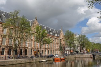 Historic buildings and boats along a canal, trees and cloudy sky, Amsterdam, Netherlands