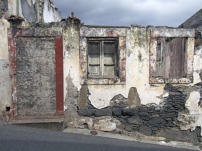 An old ruined house partly collapsed on a sloping street with a blocked up door crumbling walls and