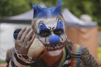 A clown with a microphone and striking make-up, menacing atmosphere outdoors
