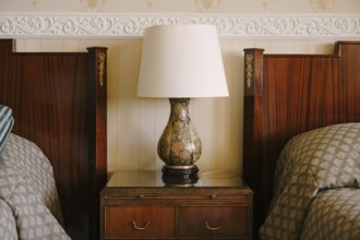 Bedside lamp on the nightstand. Refined and rich interior. Wooden bedside table next to two beds.