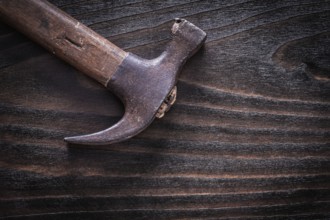 Rusty metal claw hammer on vintage dark wooden board top view construction concept