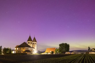 Church of St Peter and St Paul under a purple starry sky with aurora borealis, surrounded by fields