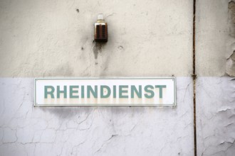 A close-up of a warning light with a rusty siren and a sign on the wall of an industrial ruin