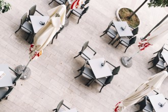 Top view of tables and chairs near folded beach umbrellas on tiles.