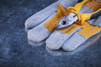 Protective gloves with pliers on scratched metallic background construction concept