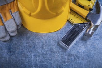 Square ruler safety gloves tape-measure building helmet and claw hammer on scratched metallic