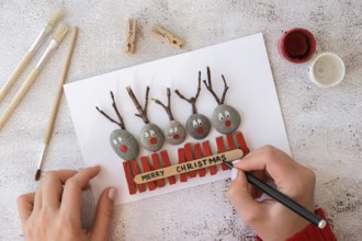 Diy Merry Christmas deer on greeting card postcard made of pebbles, sea stones, clothespins and