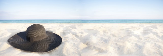 Banner Black hat on a background of the sea. Beach accessory on white sand. Straw panama on the