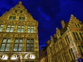 Two illuminated historical buildings at night, glowing in blue light. Cloudy sky, Ghent, Belgium,