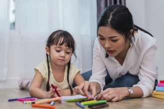 Mother teaching girl in drawing class. Daughter painting with colorful crayon color in home.