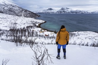 A woman in winter clothing stands above the small bay of Skjellvika on the island of Kvaloya,