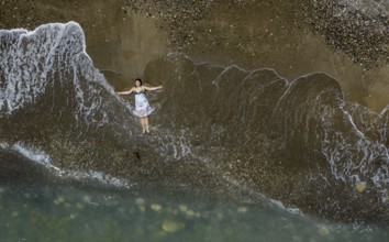Woman with swimsuit and white dress resting on a sandy beach with breaking waves on the shore.