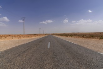An endless desert highway and power lines leading through the rock and sand desert of southwestern