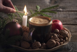 Christmas cozy atmosphere with a woman lighting a candle on a wooden platter full with nuts, apples