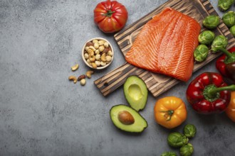 Fresh raw salmon fillet on wooden cutting board, organic bio vegetables and nuts on rustic stone