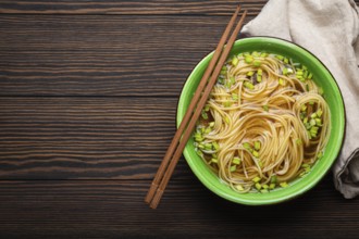 Asian noodles soup in green rustic ceramic bowl with wooden chopsticks top view on dark wooden
