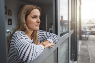 Young blonde caucasian woman looking out the window of her dorm room getting some fresh air on a