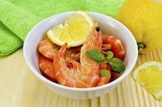 Raw shrimp in a white bowl with lemon, basil and green cloth on a wooden board