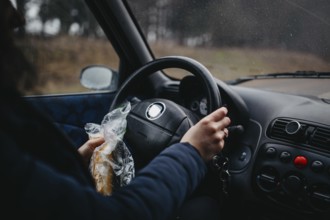 Person holding a sandwich and steering wheel in a car, capturing a casual driving moment