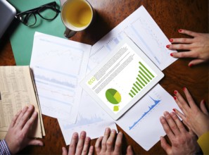 Business team hands at work with financial reports and a tablet computer, top view