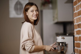 Woman smiling while using an espresso machine next to a brick wall