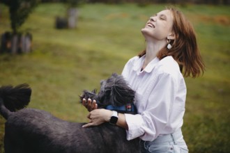 A woman laughing joyfully with a dog in a park, epitomizing happiness and connection