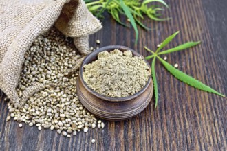 Hemp flour in a clay bowl, the grain in the bag and on the table, green cannabis leaf on a
