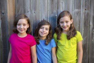 Sister and friends kid girls portrait smiling happy on gray fence wood backyard