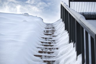 Winter scene where a set of stairs is almost completely covered in snow and railing on the right