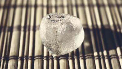 Ice cube on the wooden surface shined by the sun
