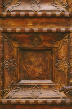Close-up texture of brown wooden doors with raised carvings and square patterns.