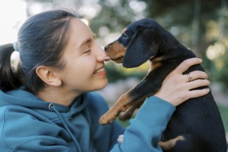 Black puppy licks the nose of a smiling girl holding him in her arms.