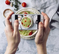 Woman hands takes top view photography of zucchini noodles salad on table with phone. Smartphone