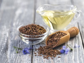 Flax seeds and flax oil. Brown linen seeds, flaxseed oil and blue flax flowers on old gray wooden