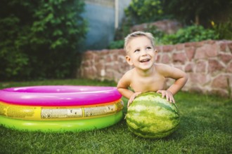 Toddler cute Caucasian white European race boy sitting hugging holding huge watermelon and smiling